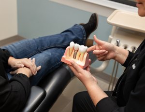 Dentist holding a dental implant model to demonstrate dental implant placement and restoration to a patient